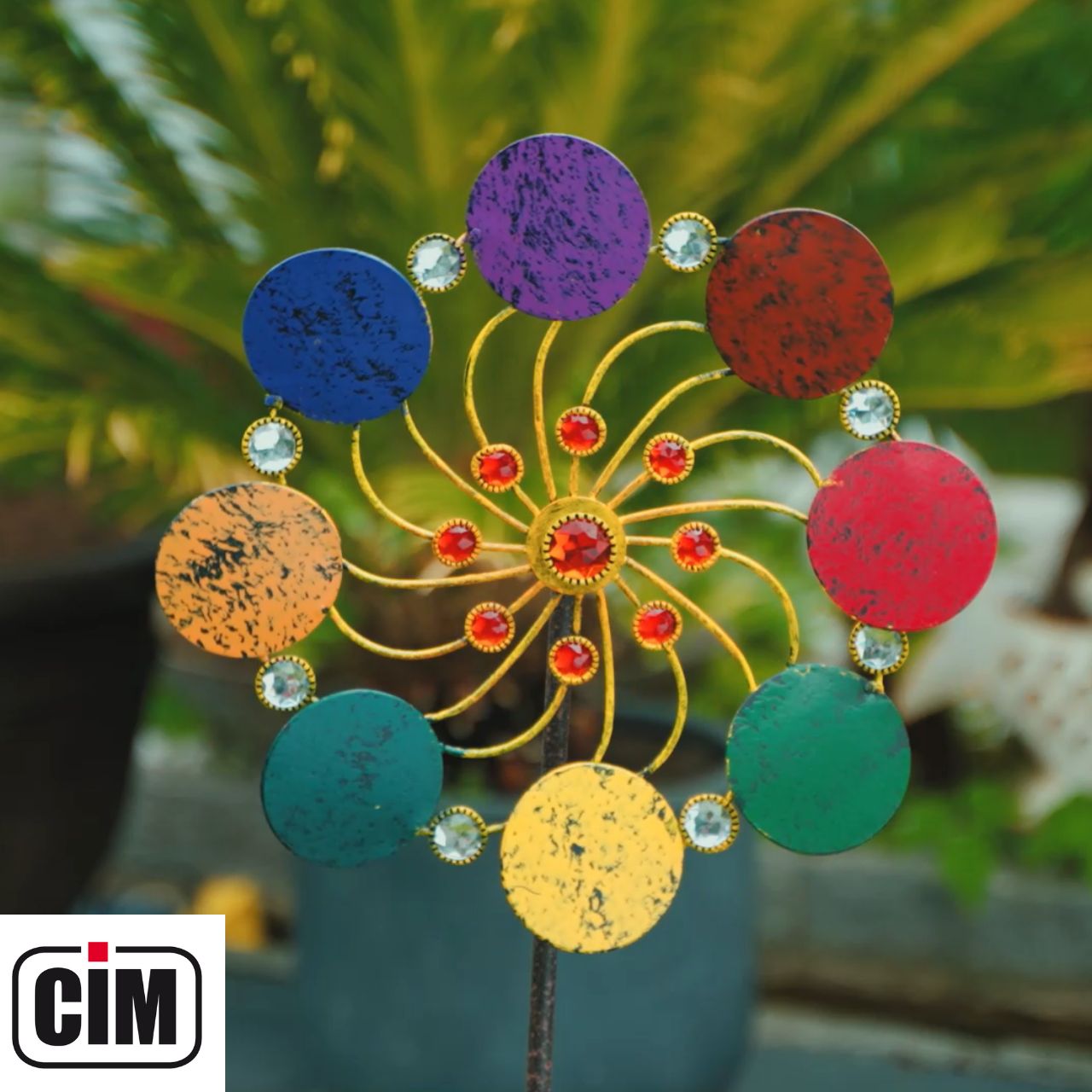 Handgefertigtes Regenbogen-Windrad aus Metall platziert als Gartendekoration in einem grünen Blumenbeet.
