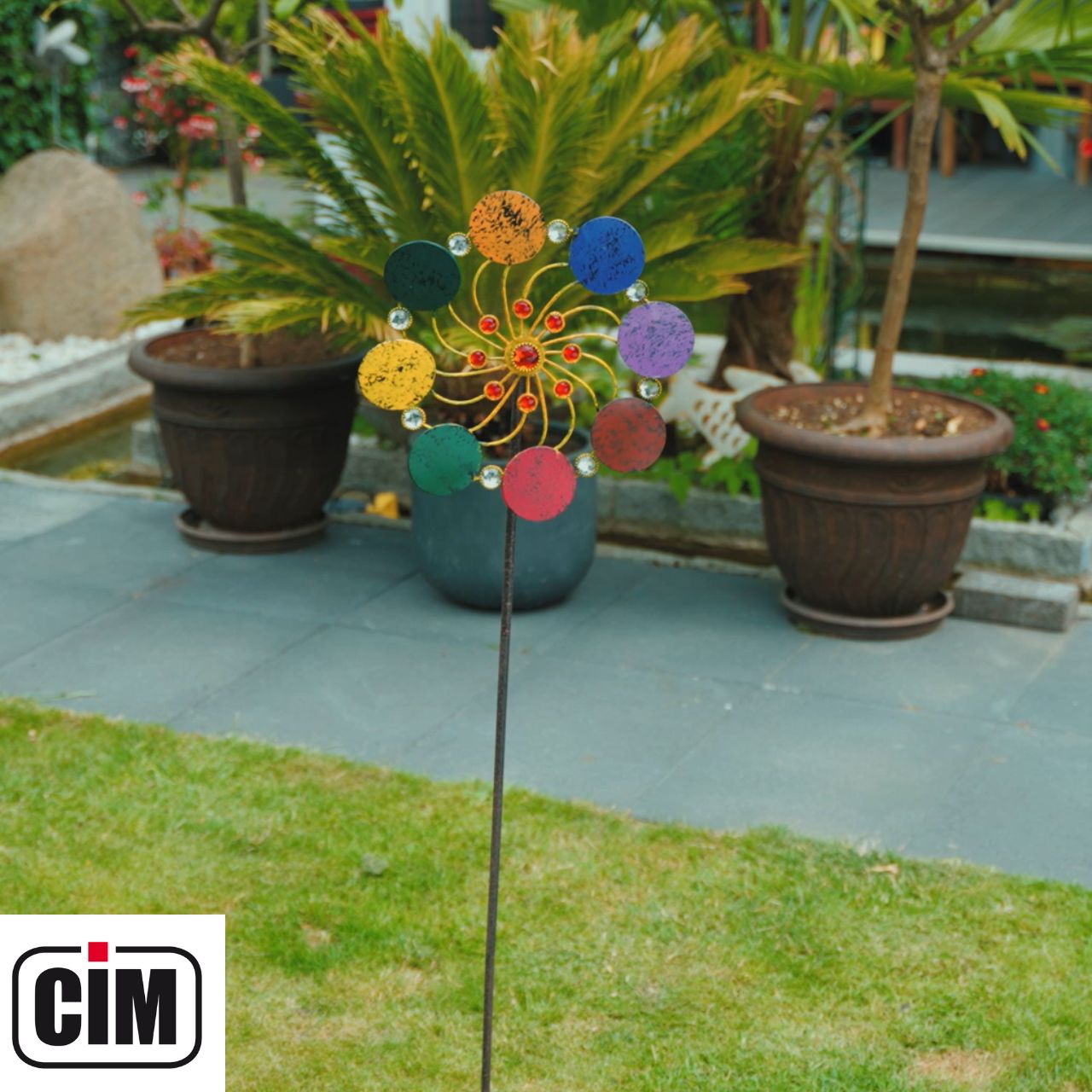 Handgefertigtes Regenbogen-Windrad aus Metall platziert als Gartendekoration in einem grünen Blumenbeet.
