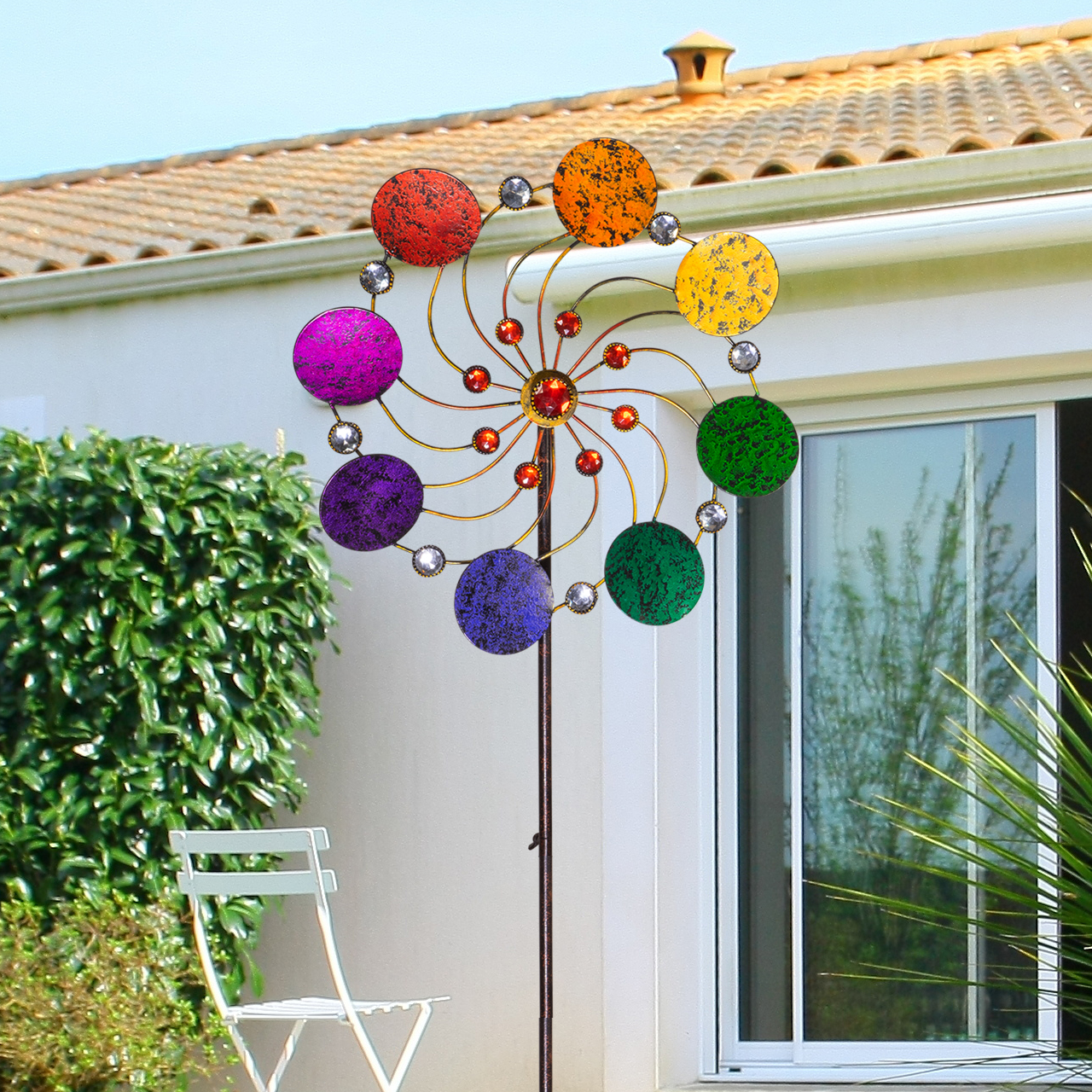 Handgefertigtes Regenbogen-Windrad aus Metall platziert als Gartendekoration in einem grünen Blumenbeet