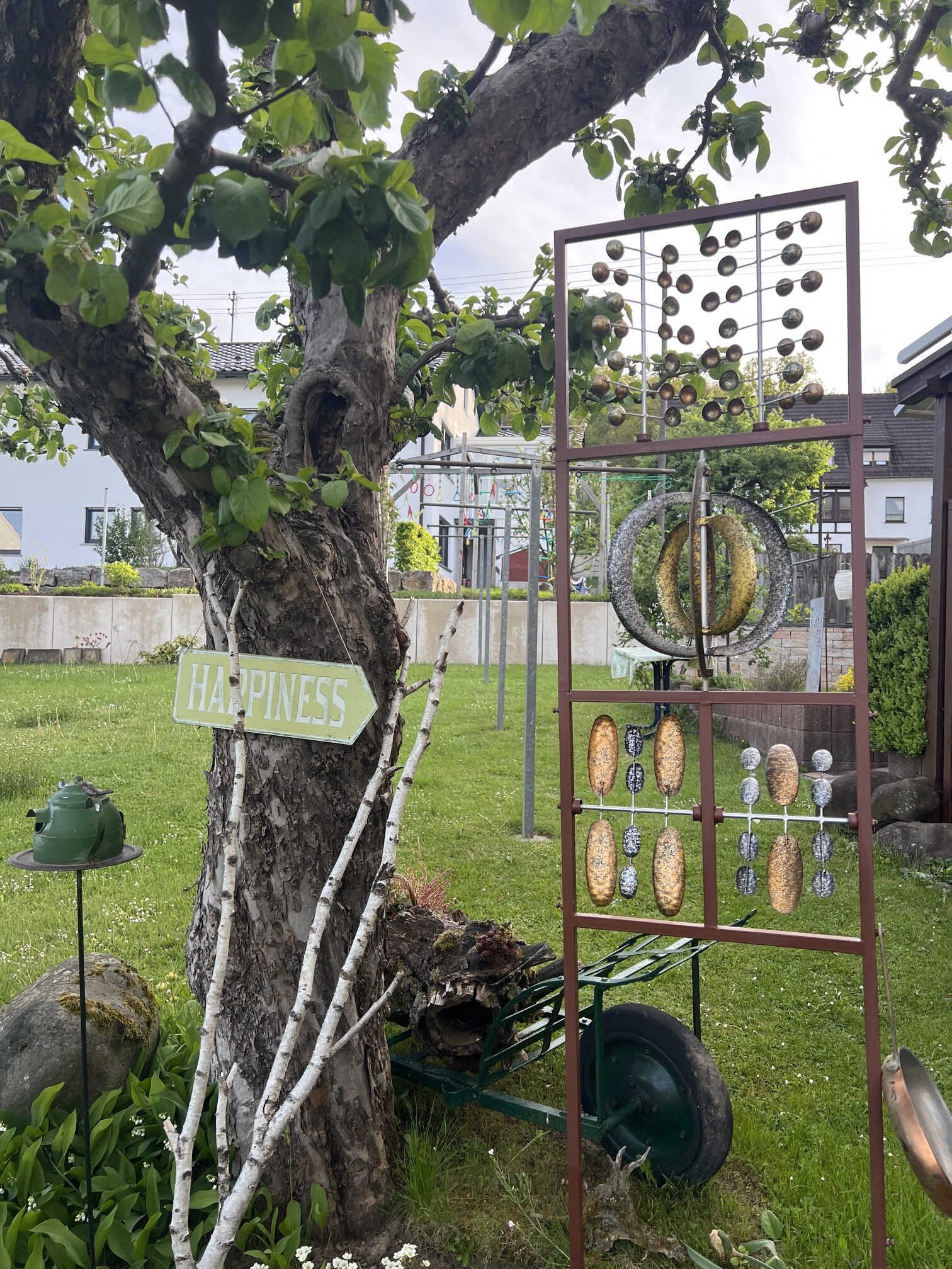 XXL Metall Windspiel Kinetic Spinner Great Wall im Garten auf grünem Rasen vor einer Hecke. Dreistufiges kinetisches Windrad mit 7 rotierenden Rädern in Bronze-Optik, Gesamthöhe 217 cm.